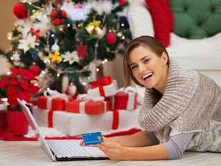 Woman with laptop near Christmas tree making online purchase