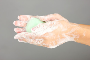 Woman's hands in soapsuds, on gray background close-up