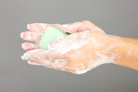 Woman's hands in soapsuds, on gray background close-up