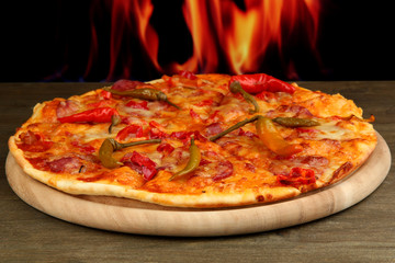 Tasty pepperoni pizza on wooden board on flame background