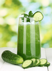 Glass of cucumber juice on wooden table, on green background