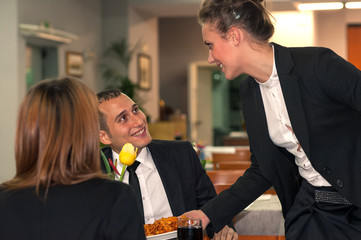 Young couple eating dinner with a waitress serving food 
