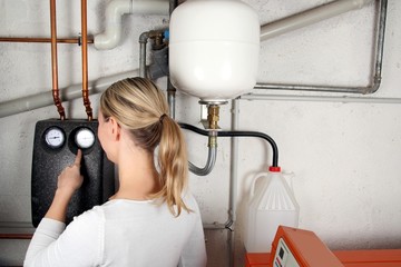 Frau prüft Wasserstand an Heizungssystem im Keller