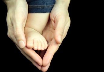 Baby foot in mother hands on black background.