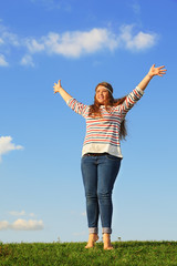 Young girl in jeans raises her hands at green grass