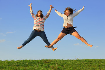 Fototapeta na wymiar Dwie młode dziewczyny skaczą na tłuszczu zielonej trawie na tle nieba