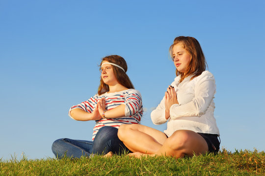 Two young girls meditate and reflect at green grass