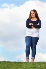 Young fat girl stands at green grass and crosses her arms