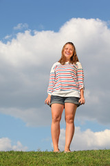 Young fat girl in shorts stands at green grass and laughs