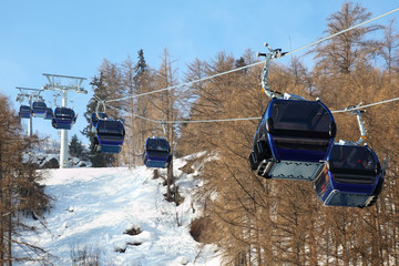 Ski chair-lift with skiers in forested mountains in  Alps