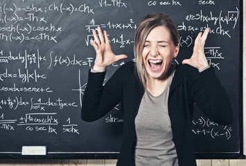  stressed professor screams and holds her head, in class with blackboard in the background. difficulties at work and communication.