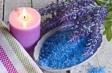 Sea salt in bowl with candle and towels on blue wooden backgroun
