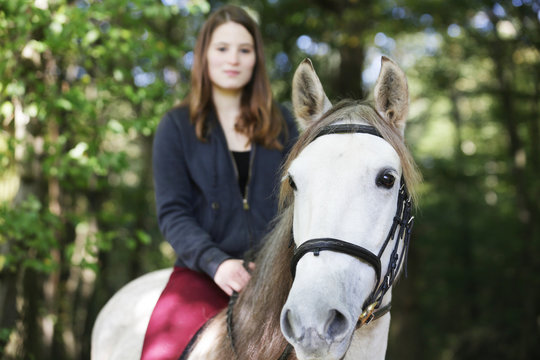 junges mädchen reitet auf weißem pferd im wald