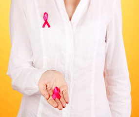 Woman with pink ribbon in hands on orange background
