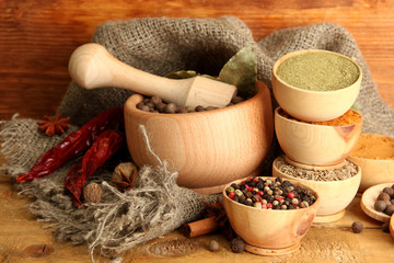 mortar, bowls and spoons with spices, on wooden background