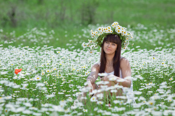 Fototapeta premium Young woman in camomile wreath looking at camera smiling