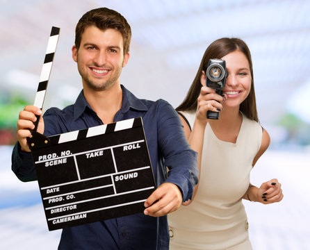 Man Holding Clapper Board And Woman Capturing Photo
