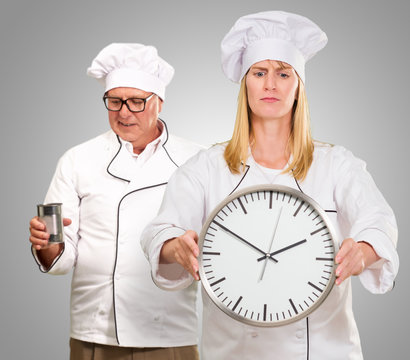 Female Chef Holding Clock In Front Of Male Chef