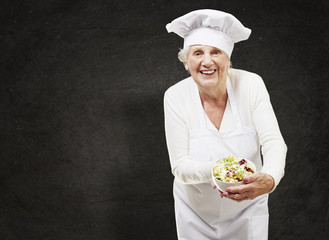 senior woman cook holding a bowl with salad against a grunge bac
