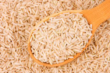 Raw brown rice in wooden spoon on rice background