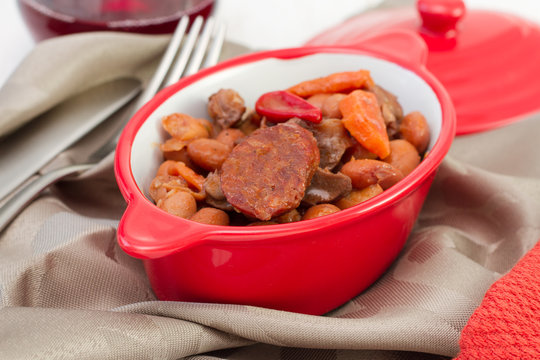 chorizo with beans in sauce in the red bowl