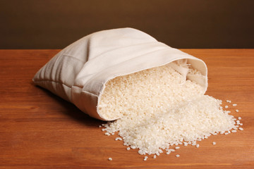 Cloth bag of rice on wooden table on brown background
