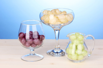 Color candies in glasses on wooden table on blue background