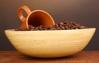 Coffee beans in bowl with cup on table on brown background