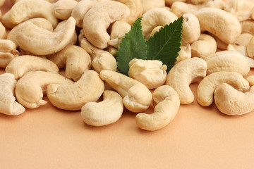 tasty cashews nuts with green leaves, on beige background