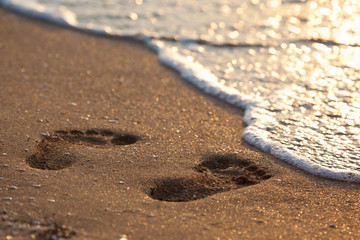 Fototapeta na wymiar Ślady stóp na piasku, wkrótce być myte avay pienisty białą falę