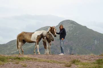 Young girl caresses two free horses in the mountains