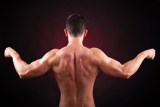 Muscular young man from back on black background