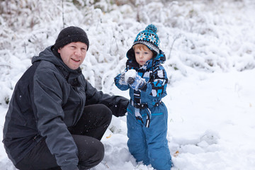 Fototapeta na wymiar Father and toddler boy having fun with snow on winter day