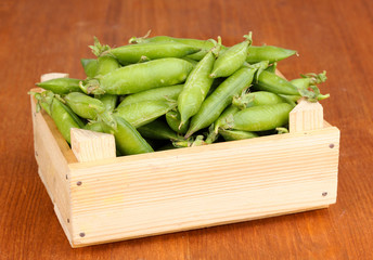 Green peas in crate on wooden background