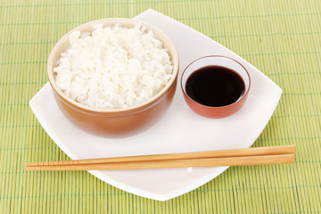 Bowl of rice and chopsticks on plate on bamboo mat