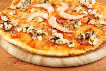 Delicious pizza with seafood on stand on wooden background