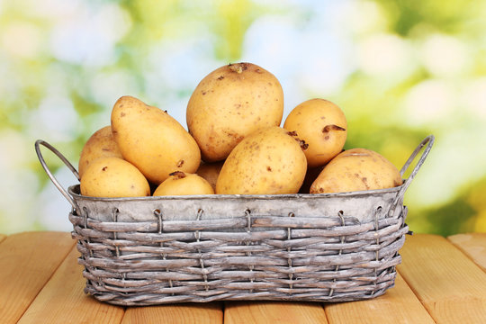 Ripe potatoes on basket on wooden table on natural background