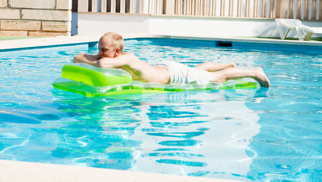 Junger mann auf einer grünen luftmatratze in einem schwimmbad