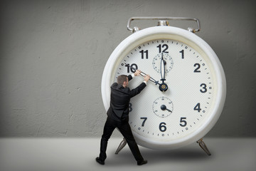 Businessman pulling a clock hand backwards - obrazy, fototapety, plakaty