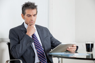 Contemplative Businessman Using Digital Tablet In Office