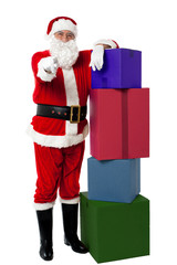 Santa posing beside colorful stack of Xmas presents