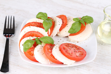 Tomato and mozzarella with basil leaves on a white plate