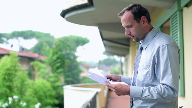 Businessman doing his finances with cellphone on his balcony 