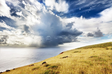 Clouds over sea and green hill in Easter Island