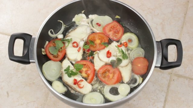 fish fillet fried with fresh herbs in a pan