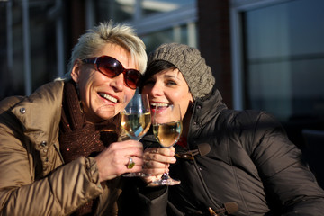 Zwei lächelnde Frauen geniessen die Sonne bei einem Glas Wein