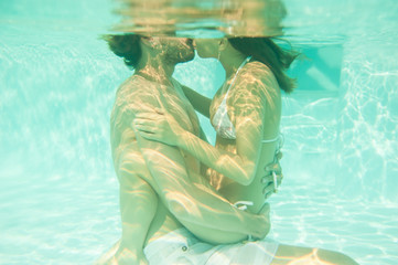 loving couple hugs, kisses and swims underwater in the pool under the open sky