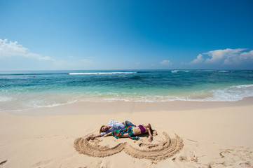 Fototapeta na wymiar loving couple resting on the beach in Bali. Heart in the sand