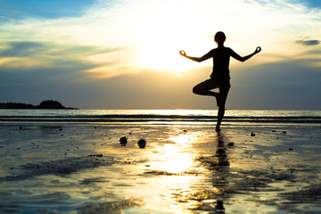 Fototapeta na wymiar Młoda kobieta ćwiczenia jogi na plaży o zachodzie słońca