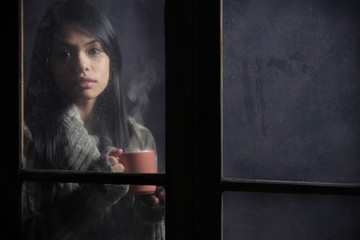 Portrait of a beautiful woman behind window with a cup of coffee
